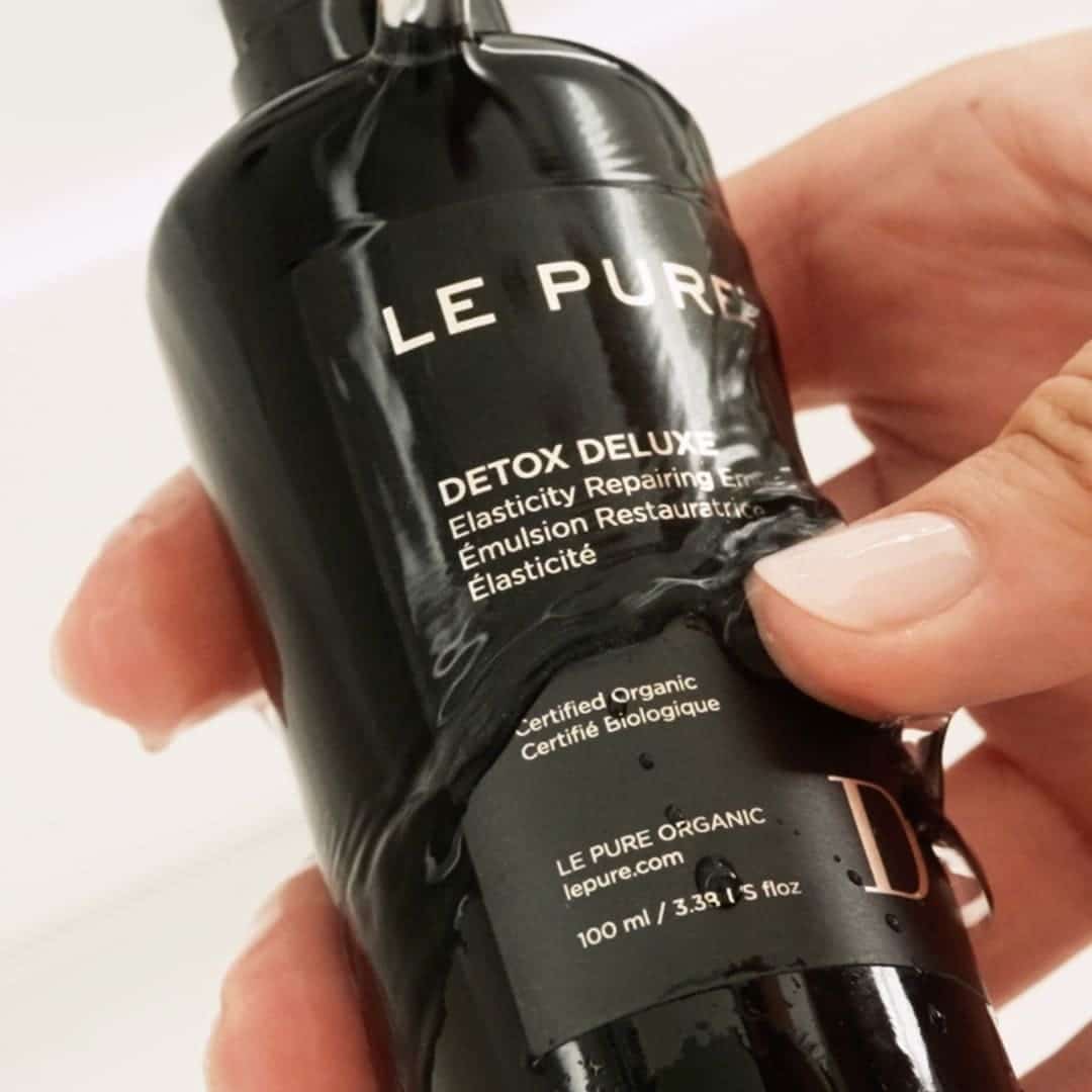 A close-up of aa hand holding a bottle of Detox Deluxe immersed in water.