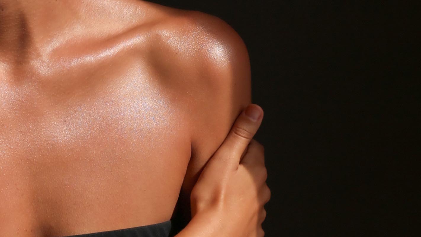 Modèle avec un décolleté bronzé et lumineux après l'application du Fluide Bronzant Éclat Naturel LE PURE Infinite Glow
