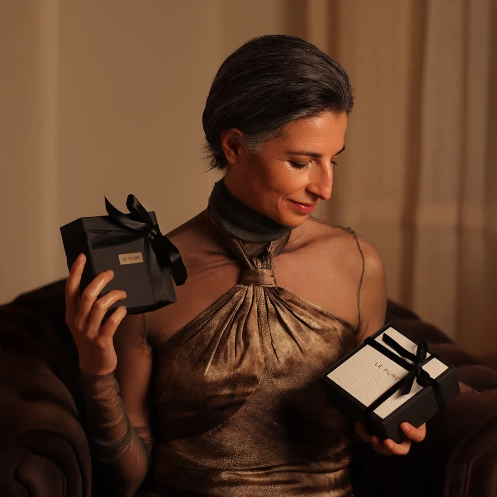 Mujer sosteniendo dos elegantes cajas de regalo negras con una sonrisa suave, evocando la calidez y la intimidad de regalar con conciencia.